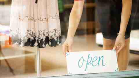 A small business owner with ADHD places a Open sign in her shop window.