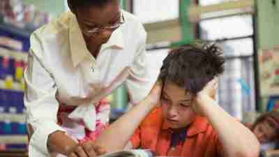 A teacher helping a child with math problems in the classroom, in accordance with his IEP