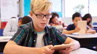 Boy with ADHD wearing glasses using tablet in elementary school class
