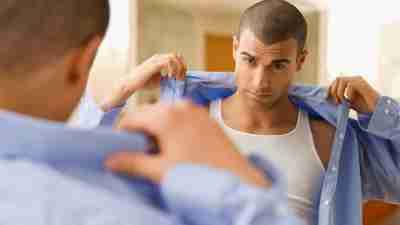 Man with mood disorder looking in mirror and putting on shirt