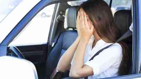 A woman covers her face with her hands in the car and wonders how to stop her anxiety