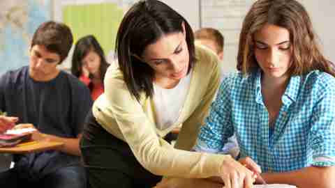 A teacher helps a girl who is struggling in class. She may have a learning disability.