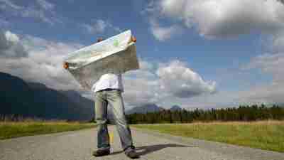 Man with ADHD standing on road holding map with mountains behind him