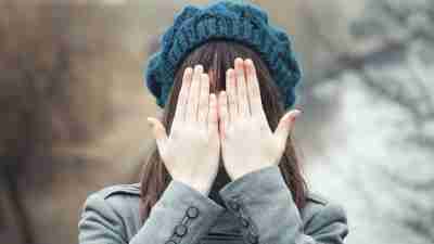 Girl with ADHD covers face with hands outside