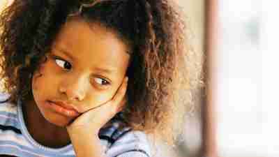 A sad girl with a hand on her face has Bipolar Disorder, which can occur in children with ADHD