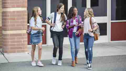 Four happy teen girls talking as they leave school. Happiness and emotional health are vital for teen girls with ADHD, who struggle with emotional dysregulation, rejection sensitive dysphoria, and hormonal fluctuations.