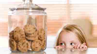 Girl mischievously stares at a cookie jar on the counter.