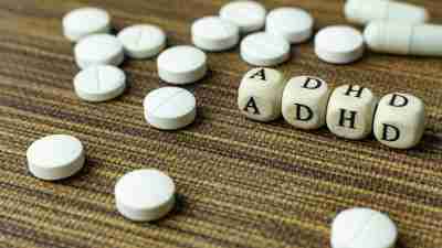 Lettered dice arranged to spell "ADHD" with generic medication pills around