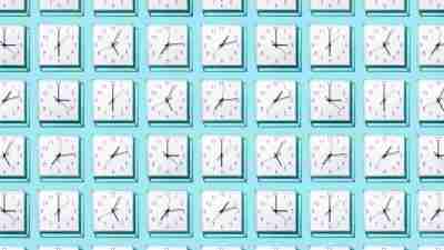 Neatly Arranged White Colored Wall Clocks Displays Different Time on Solid Blue Background.