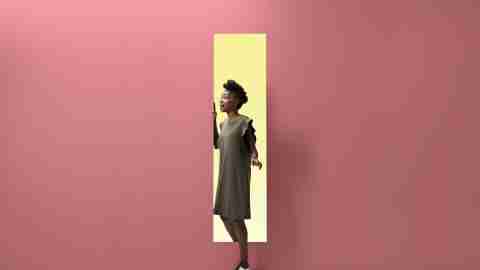 Woman walking out of rectangular opening of coloured wall