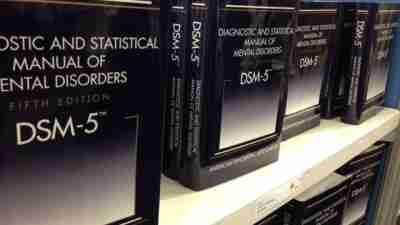 For-sale DSM-5 manuals are organized in rows and standing upright on a white shelf against a blue wall.