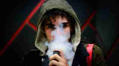 teenage boy vaping with face partially covered from smoke