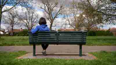 ADHD Woman sitting on bench with back turned looking at the park thinking