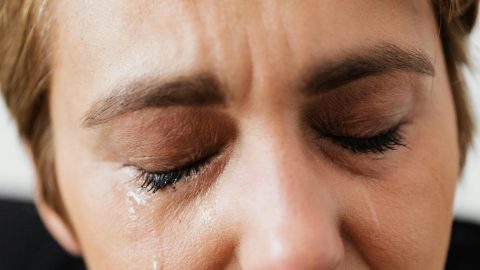 A closeup of a woman with closed eyes, a tear streaming down her face.