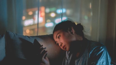 A tired woman resting on her couch while looking at her phone