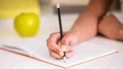 Girl with ADHD writing in notebook with apple beside her trying to prepare for class