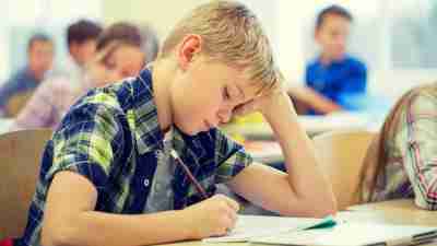 Young boy with ADHD taking test in classroom filled with students