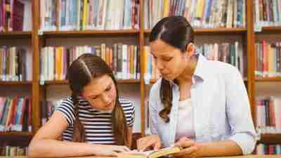 A young girl with ADHD and her tutor working in the library