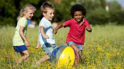 Three children with ADHD playing with beach ball in field outside, well-behaved thanks to a new ADHD medication